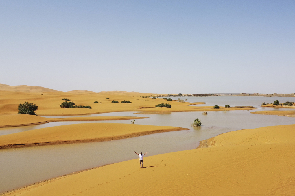 Người đàn ông đi cạnh hồ nước do mưa lớn tạo ra giữa những cồn cát ở Merzouga. Ảnh: AP